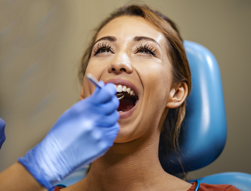Woman receiving dental examination from dentist wearing blue gloves in dental office chair.