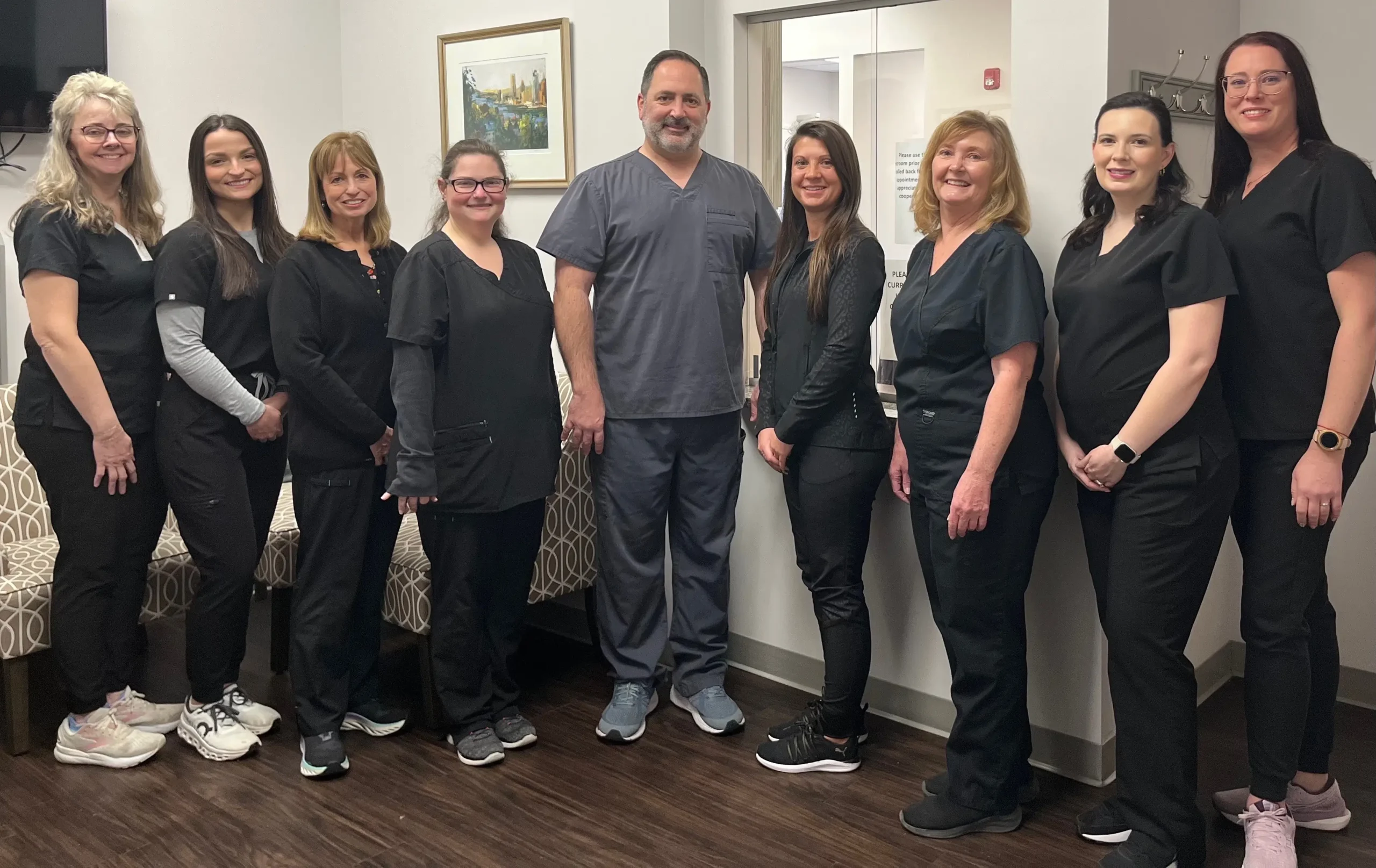 McMurray Family Dental team members posing together in dental office hallway wearing black scrubs.