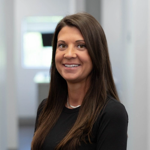 Professional woman smiling at camera in modern dental office setting wearing black top.