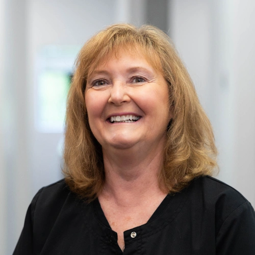 Woman with reddish-blonde hair smiling at camera in professional dental office setting.