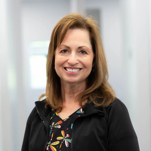 Woman smiling at camera wearing black jacket in dental office setting.