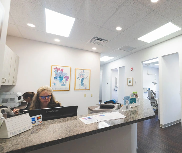 Dental receptionist at front desk in modern, clean office with colorful artwork on walls.