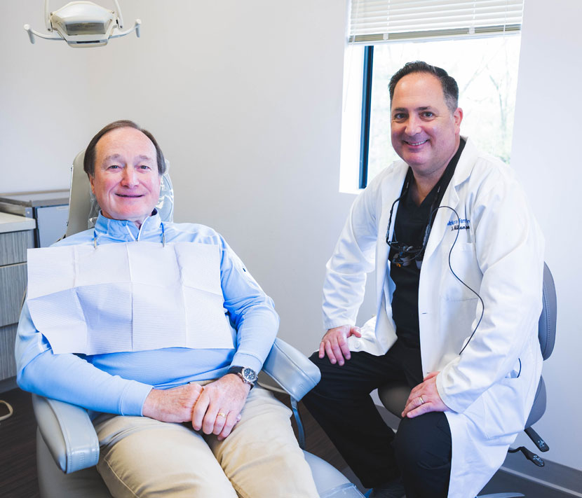 Dentist in white coat beside patient in dental office examination room.