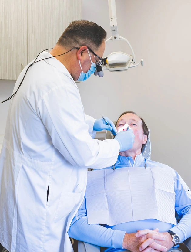 Dentist in white coat examining patient's teeth in modern dental office with overhead light.