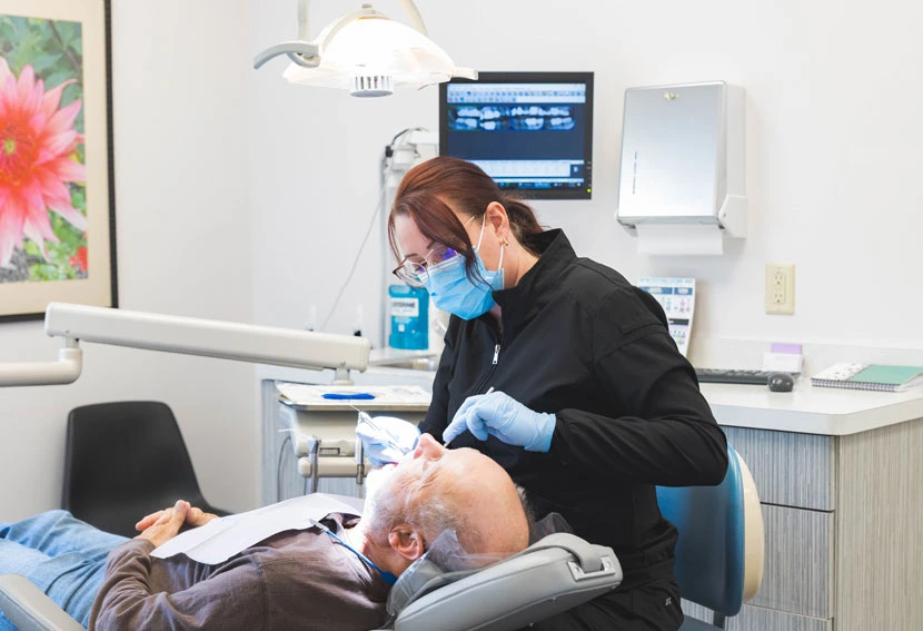 Dentist examining patient in dental chair while assistant monitors treatment in modern office.