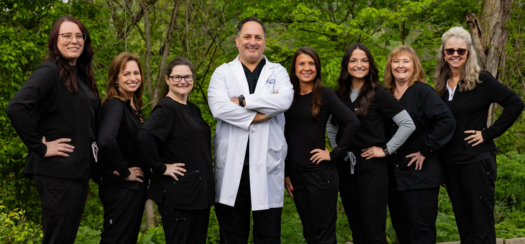 McMurray Family Dental team of eight dental professionals in black attire posing outdoors.