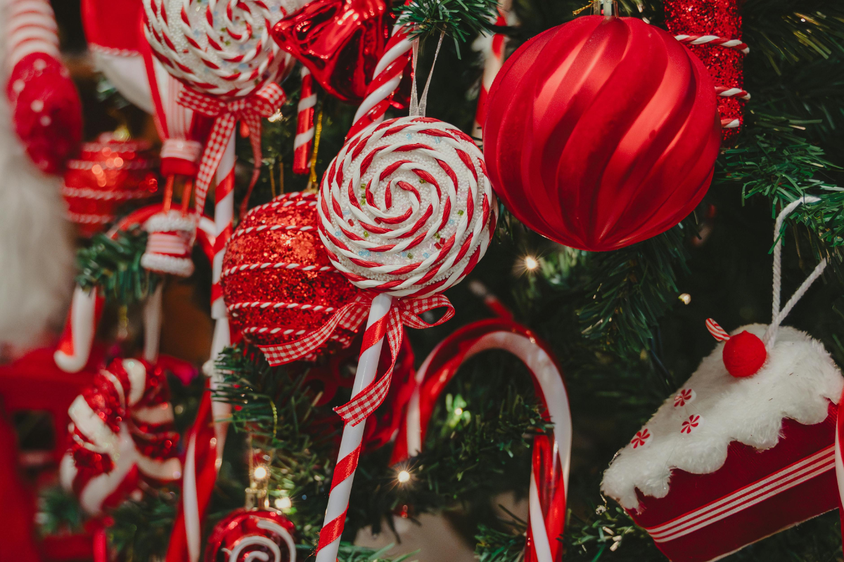 Red and white Christmas ornaments, candy canes, and lollipops decorating evergreen branches.